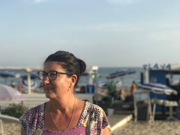 Mature woman wearing eyeglasses at beach against sky