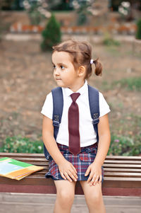 Little cute schoolgirl in uniform sitting on a bench and laughing