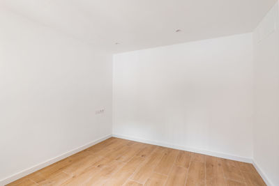 Empty room with laminate flooring and newly painted white wall in refurbished apartment. 