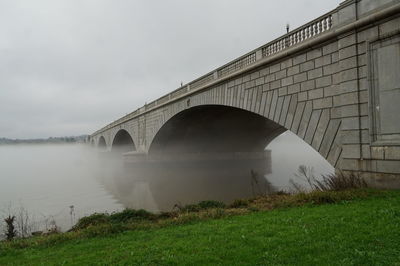Arch bridge over river during foggy weather