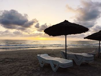 Lounge chairs and umbrellas on beach against sky during sunset