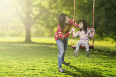 Mother pushing daughter on swing in park