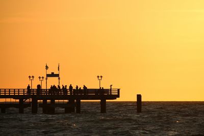 Silhouette built structure on sea against orange sky