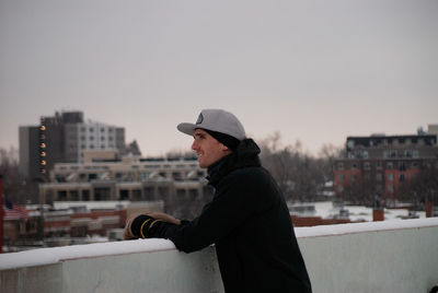 Side view of man standing in city against sky during winter