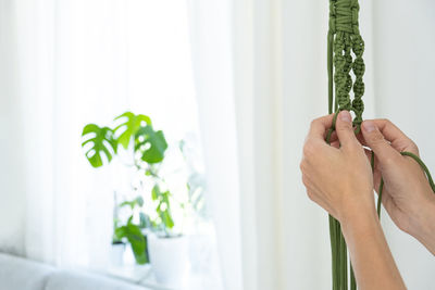 Handmade green macrame plant hangers with potted plant are hanging on woman hand. pot and monstera