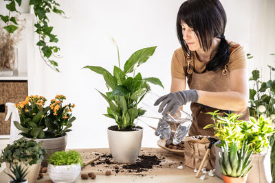 Portrait of young woman standing by potted plant on table at home