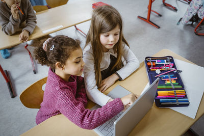 High angle view of schoolgirls using laptop together at desk in classroom