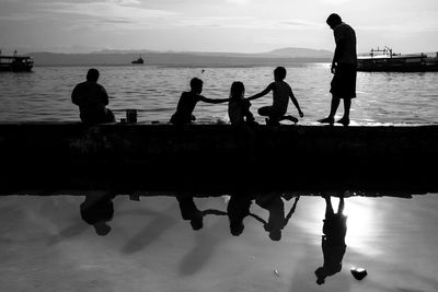 Silhouette people by sea against sky during sunset