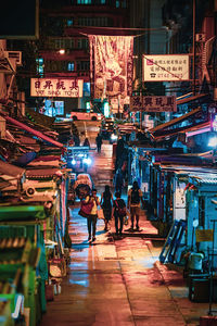 People walking on illuminated street market in city at night
