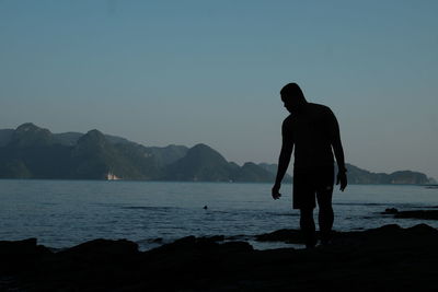 Silhouette man standing by sea against clear sky