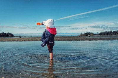 Side view of girl playing in water against sky