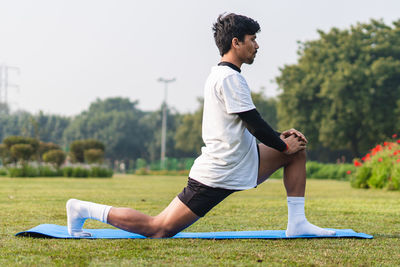 Young indian boy stretching in the park, young sportsman stretching his body and working  out.