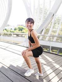 Happy young sportswoman standing at footpath on sunny day