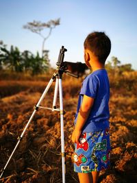 Side view of boy standing by tripod on field