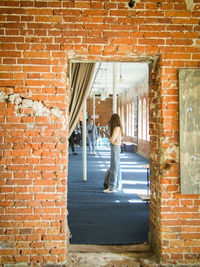 Rear view of woman standing against brick wall