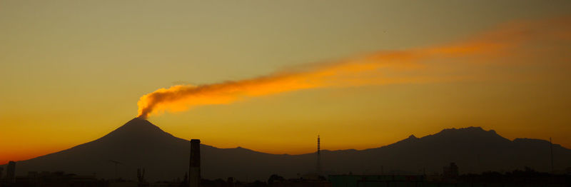 Scenic view of silhouette volcan in eruption against sunset sky