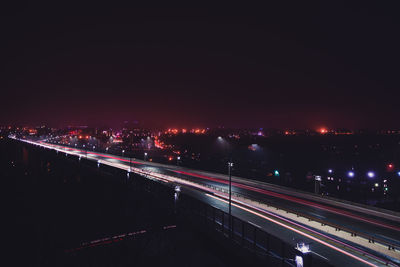 Light trails on illuminated city against sky at night