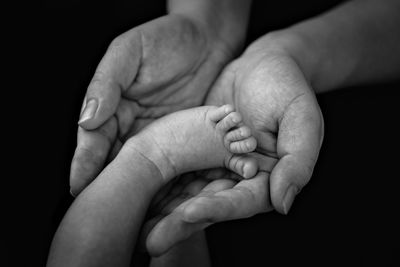 Close-up of father holding baby foot against black background