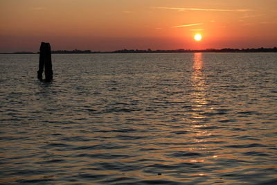 Silhouette person standing in sea against sky during sunset