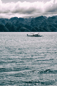 Sailboat sailing on sea by mountains against sky