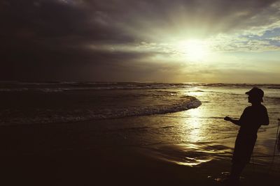 Rear view of silhouette woman standing at beach during sunset