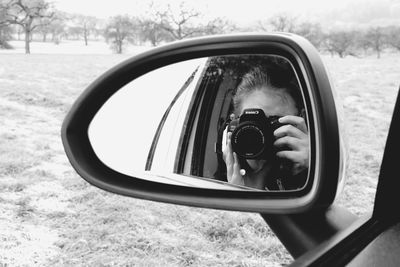 Reflection of boy photographing on side-view mirror