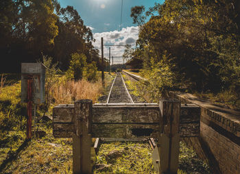 Abandoned railroad tracks by trees against sky