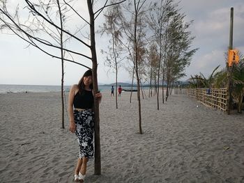 Full length portrait of woman standing by tree at beach