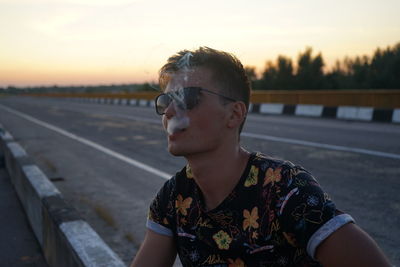 Portrait of teenage girl standing on road against sky during sunset