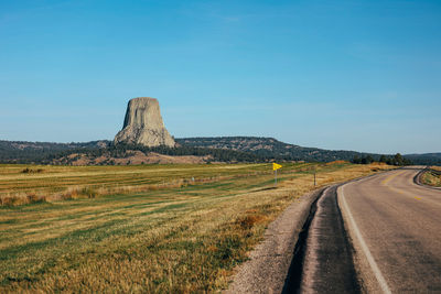 Road amidst field against clear blue sky