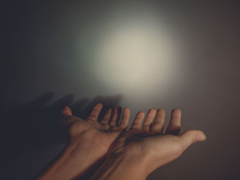 Cropped image of woman gesturing against light on wall