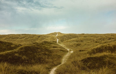 Footpath on grassy field against sky