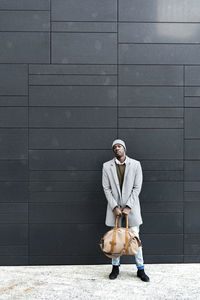 Businessman holding duffel bag standing in front of black wall