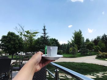 Midsection of person holding drink against sky