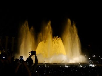 People photographing illuminated fountain against clear sky at night