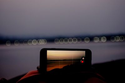 Man photographing illuminated smart phone against sky