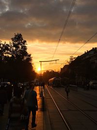 People on railroad tracks against sky during sunset