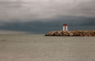 Lighthouse on beach against cloudy sky