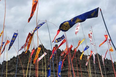 Low angle view of various flags waving at borobudur against cloudy sky