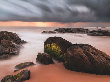 Rocks on sea shore against sky during sunset