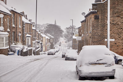 Snow covered street amidst buildings in city