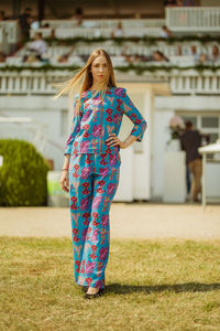 Portrait of young woman standing on grassy field against building