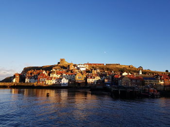 Town by river against clear blue sky