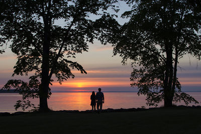 Silhouette couple at lakeshore against sky during sunset
