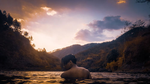 Man sitting on mountain against sky during sunset