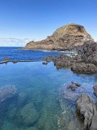 Rock formations in sea against clear blue sky