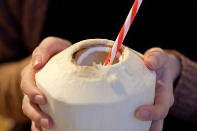 Midsection of woman holding coconut with drinking straw