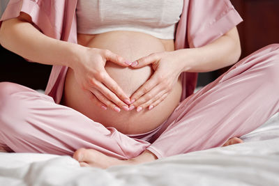 Midsection of pregnant woman touching belly sitting on bed