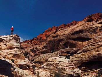 Low angle view of person standing on rock against blue sky