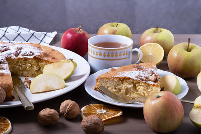 Large serving of apple pie with walnuts surrounded by ripe apples. a piece of cake on plate and tea 